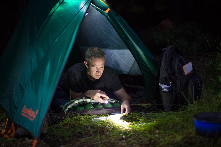 guy in a tent reading book with flashlight