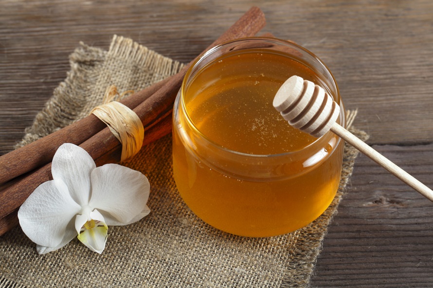 picture of honey beside a flower and cinamon sticks on a wooden table