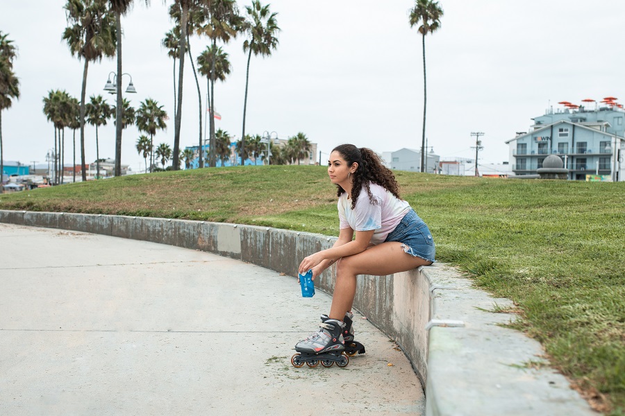 picture of a woman sitting on a wall beside a grass wearing womens inline skates