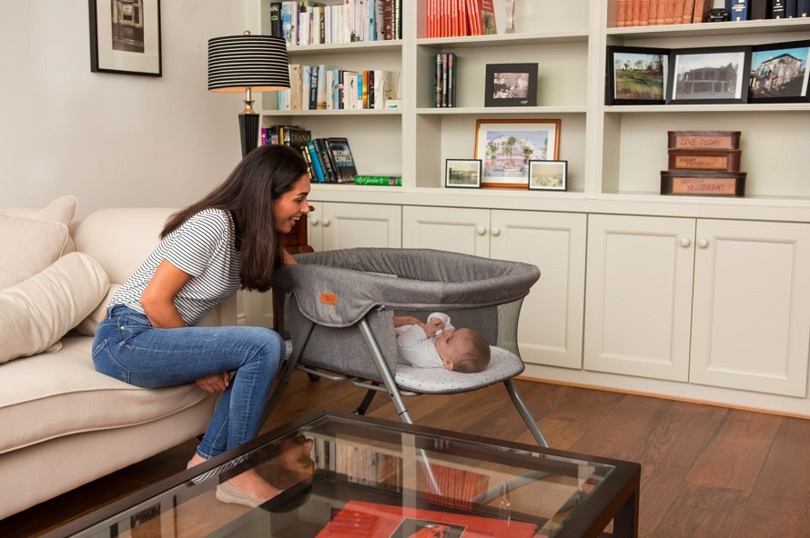 picture of a woman beside a baby in a travel cot in a living room