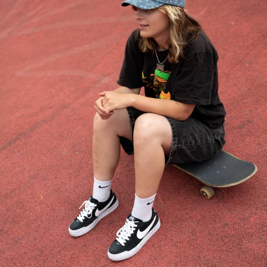 girl wearing nike sb shoes sitting on her skateboard 