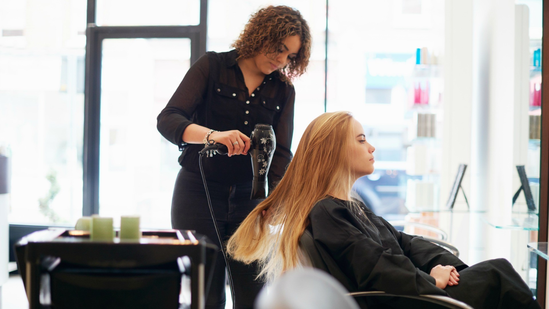 Hairdresser blow-drying a woman's hair in a salon.