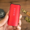 Close-up of a red Davinci vaporizer held in a hand, with accessories and herbs in the background