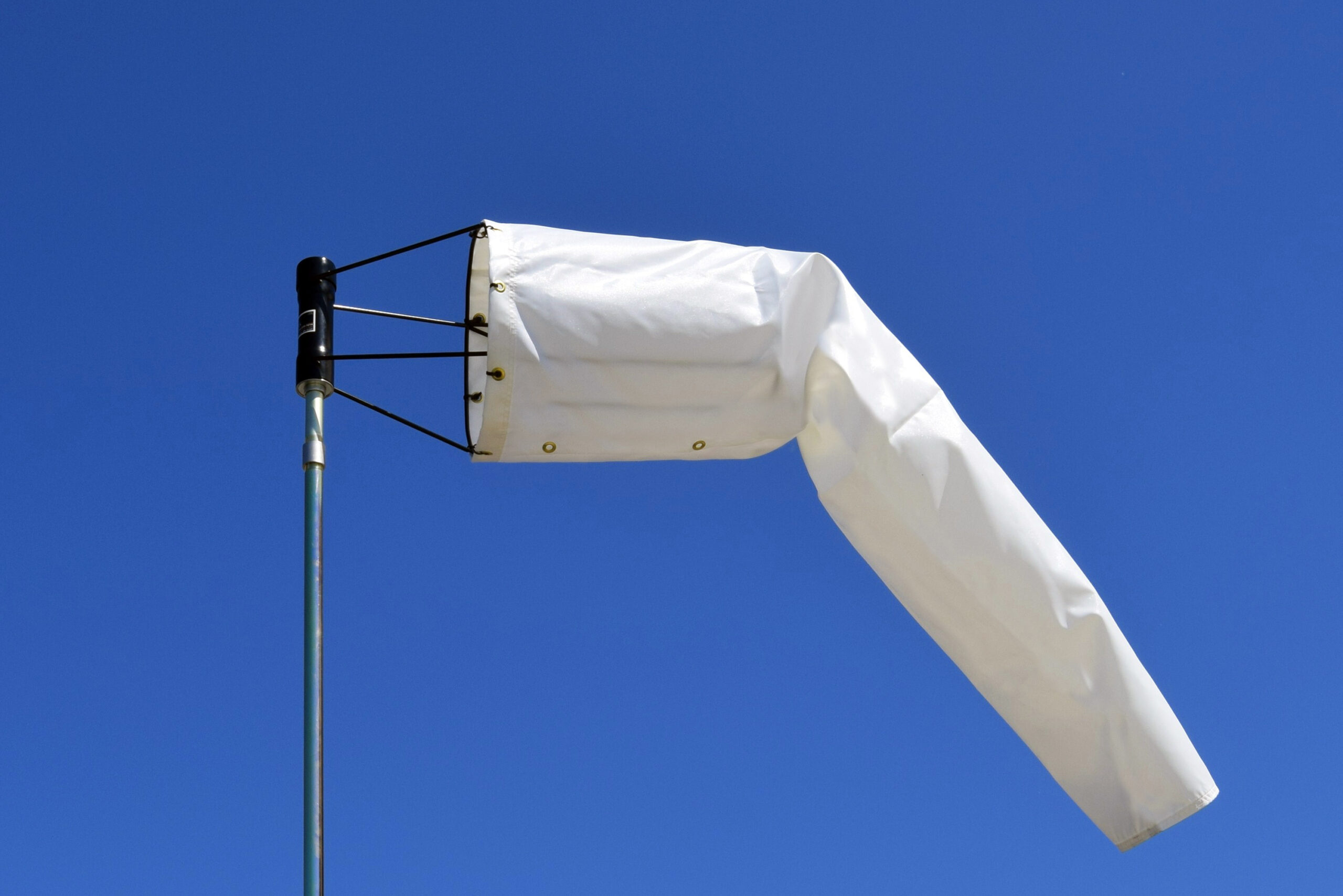 White heavy-duty windsock against a clear blue sky, showing wind direction.