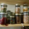 An assortment of glass jars filled with various dried foods, such as dried vegetables, herbs, and spices, organized on a wooden shelf.