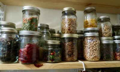 An assortment of glass jars filled with various dried foods, such as dried vegetables, herbs, and spices, organized on a wooden shelf.